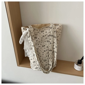 Detail of floral tote bag with a white lace bow knot on a minimalist wooden shelf