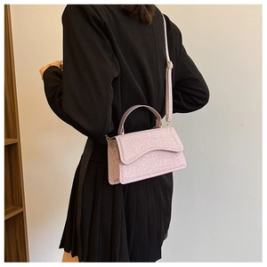 Pink glitter crossbody bag with curved flap shown on shoulder of a model in black blazer