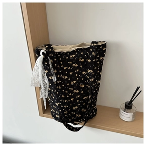 Detail of black canvas tote bag with yellow floral print and white lace bow decoration