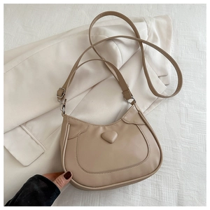Detail view of a creamy beige heart-shaped hobo bag on textured fabric background