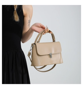 Detail of light beige leather crossbody bag with silver buckle held by a model