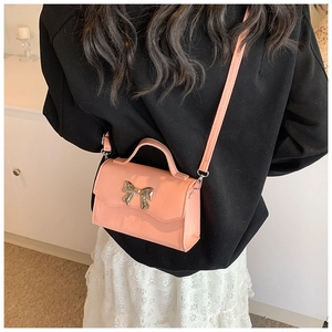 Detailed view of a pink crossbody bag featuring a shiny silver metal bow decoration
