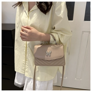 Detail of light beige crossbody bag with silver butterfly clasp and V-quilted texture