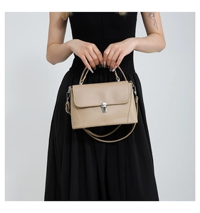 Close-up of beige underarm bag with top handle and silver buckle on black dress