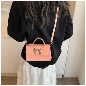 Pink crossbody bag with golden bow clasp shown on model wearing black hoodie and lace skirt