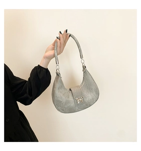 Détail d'un sac demi-lune gris avec boucle papillon argentée et texture en daim élégante