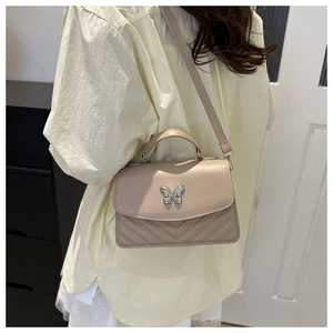 Close-up of beige crossbody bag with silver butterfly clasp and V-quilted texture