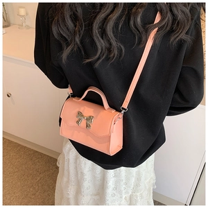 Detail of pink coral crossbody bag with golden bow and leather texture on a model