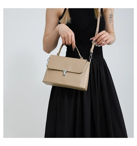 Detail of light beige crossbody bag with silver clasp lock shown on a model's outfit
