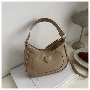 Close-up of beige leather crescent bag with heart indentation on a minimalist desk