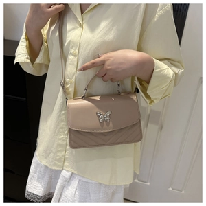 Detail of beige square handbag featuring a silver butterfly clasp and V-shaped stitching