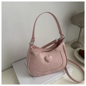 Pink PU leather crossbody bag with 3D heart detail placed on a book in soft lighting