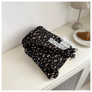 Detail of black floral tote bag with white lace trim and bow on a white table