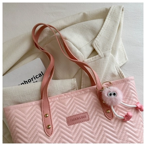 Detail of pink quilted tote bag with cute plush monster charm and leather shoulder strap