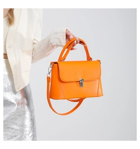 Detail of bright orange crossbody bag with silver buckle worn with silver sequin skirt