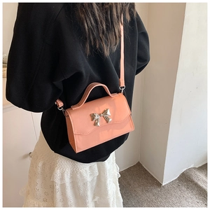Detail of coral pink crossbody bag with a silver metal bow accent on the front flap