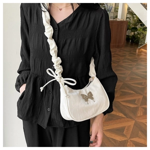Detail of white pleated shoulder strap and silver butterfly accent on crossbody bag