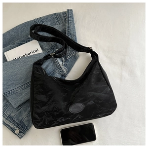 Détail du sac cabas noir plissé montrant l'écusson logo et la bandoulière réglable