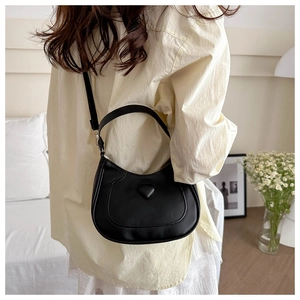 Detail of a black heart-embossed PU leather shoulder bag worn by a model in a cozy setting