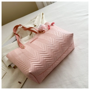 Detail of pink quilted tote bag with V-shaped stitching and plush ball charm on white fabric