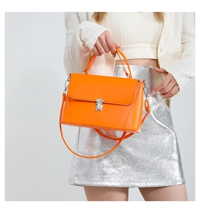 Chic orange faux leather crossbody bag with silver buckle worn with a silver skirt