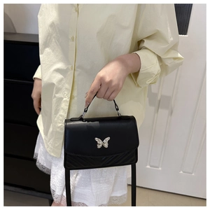 Close-up of black crossbody bag featuring silver butterfly clasp and chevron quilting