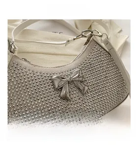 Detail of silver rhinestone shoulder bag featuring a large metallic bow and white leather strap