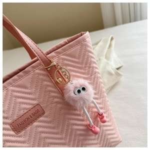 Detail of pink V-quilted tote bag with a cute plush monster charm and brand tag