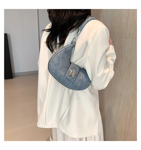Sac croissant en denim bleu avec boucle papillon dorée porté sur un blazer blanc