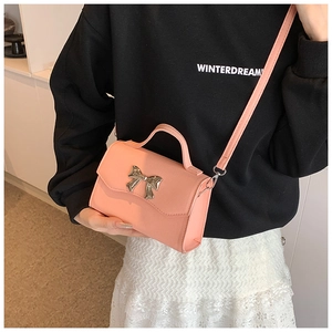 Detail of pink PU leather crossbody bag featuring a gold bow clasp and sleek top handle