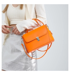 Close-up of bright orange crossbody bag featuring fine leather texture and silver buckle