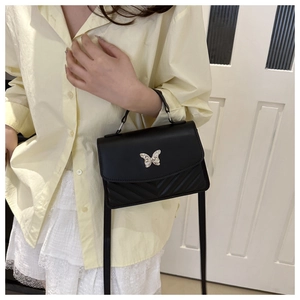 Close-up of black leather crossbody bag featuring silver butterfly buckle and V-quilted pattern