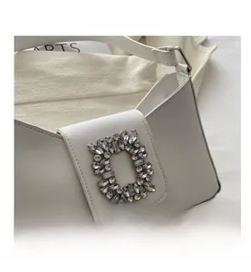 Close-up of white minimalist baguette bag featuring a large sparkling crystal buckle