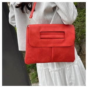 Sac bandoulière chic en cuir rouge avec chaîne porté sur une tenue grise
