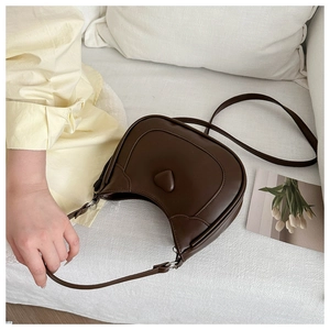 Close-up of dark brown saddle bag with heart-shaped detail and silver hardware on sofa