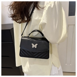 Close-up of black leather crossbody bag featuring silver butterfly buckle and V-quilt pattern
