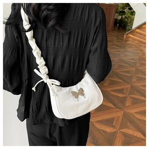 Close-up of white ruched shoulder bag with butterfly metal ornament and knotted strap