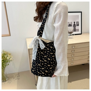 Detailed close-up of a black floral canvas tote bag featuring a white lace bow accent