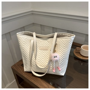 Detail of white quilted tote bag with V-pattern stitching and pink plush charm accessory