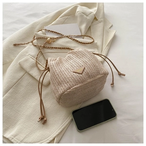 Detail of woven straw bucket bag with leather triangle badge and gold chain strap