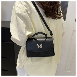 Detail of black crossbody bag with silver butterfly buckle and V-quilted faux leather