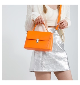 Close-up of vibrant orange crossbody bag with silver buckle on a stylish model