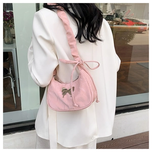 Close-up of pink shoulder bag featuring a metallic butterfly badge and scrunchie strap