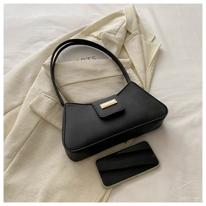 Detail of minimalist black baguette bag with gold buckle on elegant white blazer