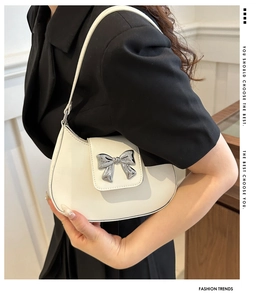 Detail of white crescent bag featuring a metallic silver bow clasp and leather texture