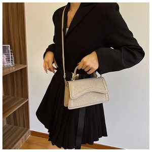 Detail of glittery gold crossbody bag with top handle worn by model in black outfit