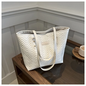 Detail of white quilted tote bag with wave pattern and metal logo plate on a desk