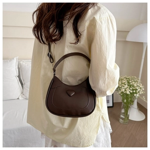 Deep brown saddle bag with heart detail worn by model in elegant home setting