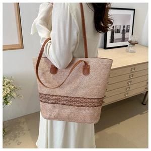 Straw tote bag with brown lace detail shown on shoulder in minimalist interior