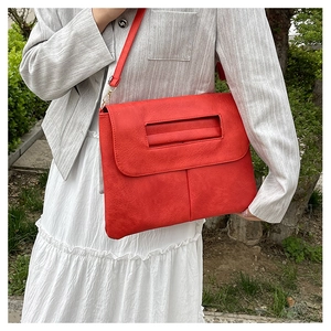 Détail d'un sac enveloppe rouge en cuir texturé avec poignée creuse et attache chaîne